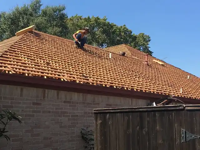 Roofer installing orange clay tile on a roof