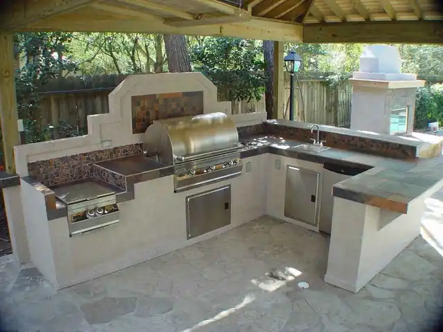 Stucco outdoor kitchen with a built-in grill and tiled counters under a covered patio in Bellaire