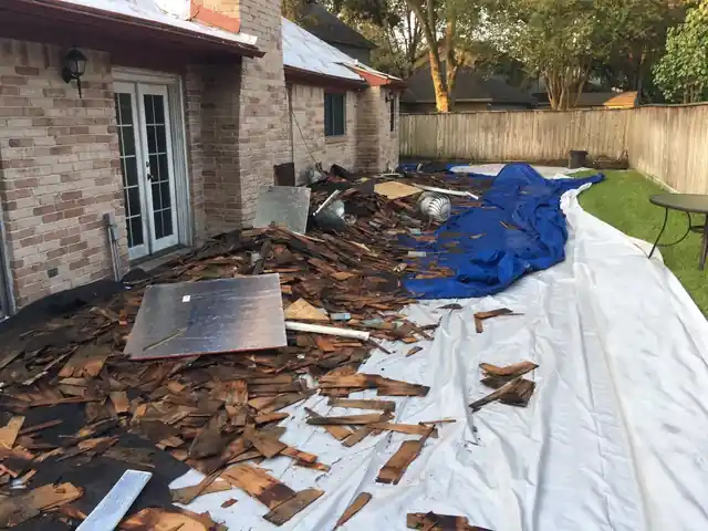 Wood shake roofing debris tarped beside a brick home during a re-deck