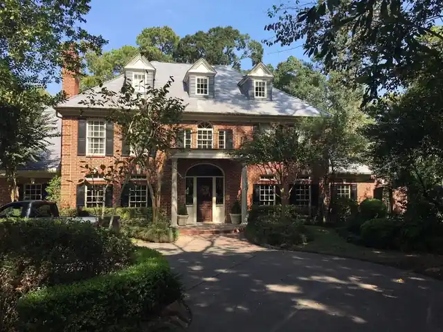 Two-storey red brick home in River Oaks with dormers and a new roof, framed by old trees